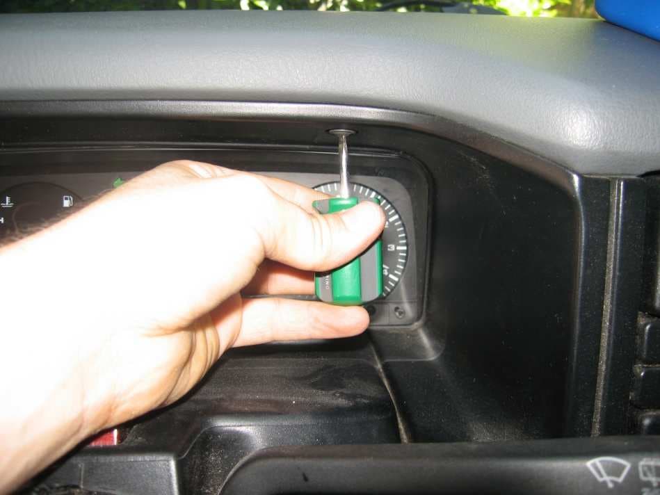 A short screwdriver undoing the top screw of the instrument cluster surround