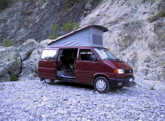 Red T4 Westfalia California with the pop-top roof raised, parked on a stony riverbed
