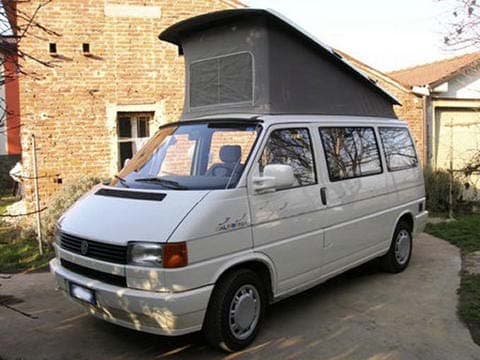 White T4 Westfalia California with the pop-top roof raised in front of a brick house