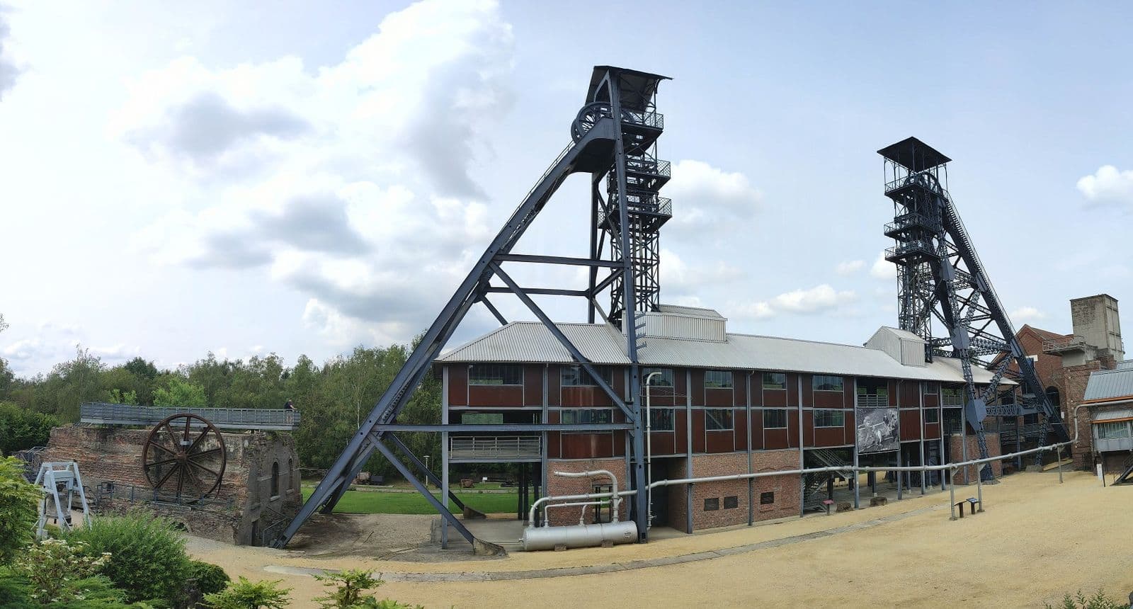 The two iron winding towers of the mine, with the large brick hall and a sky with clouds
