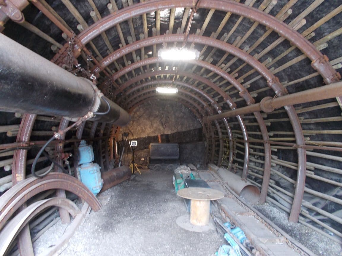 A reconstructed mine gallery with iron arches and timber, pipes and a small wooden table
