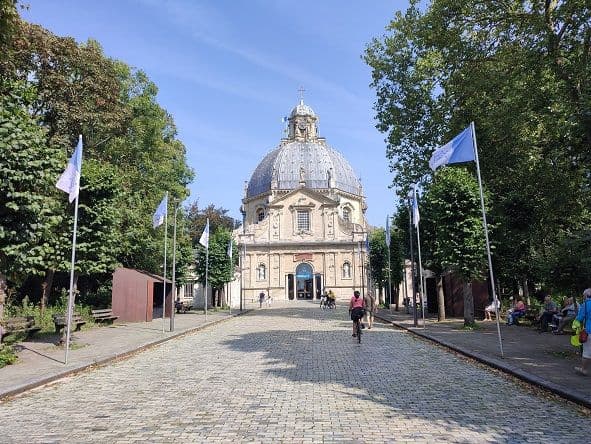 The basilica of Scherpenheuvel with its dome, at the end of the cobbled avenue lined with trees and blue flags
